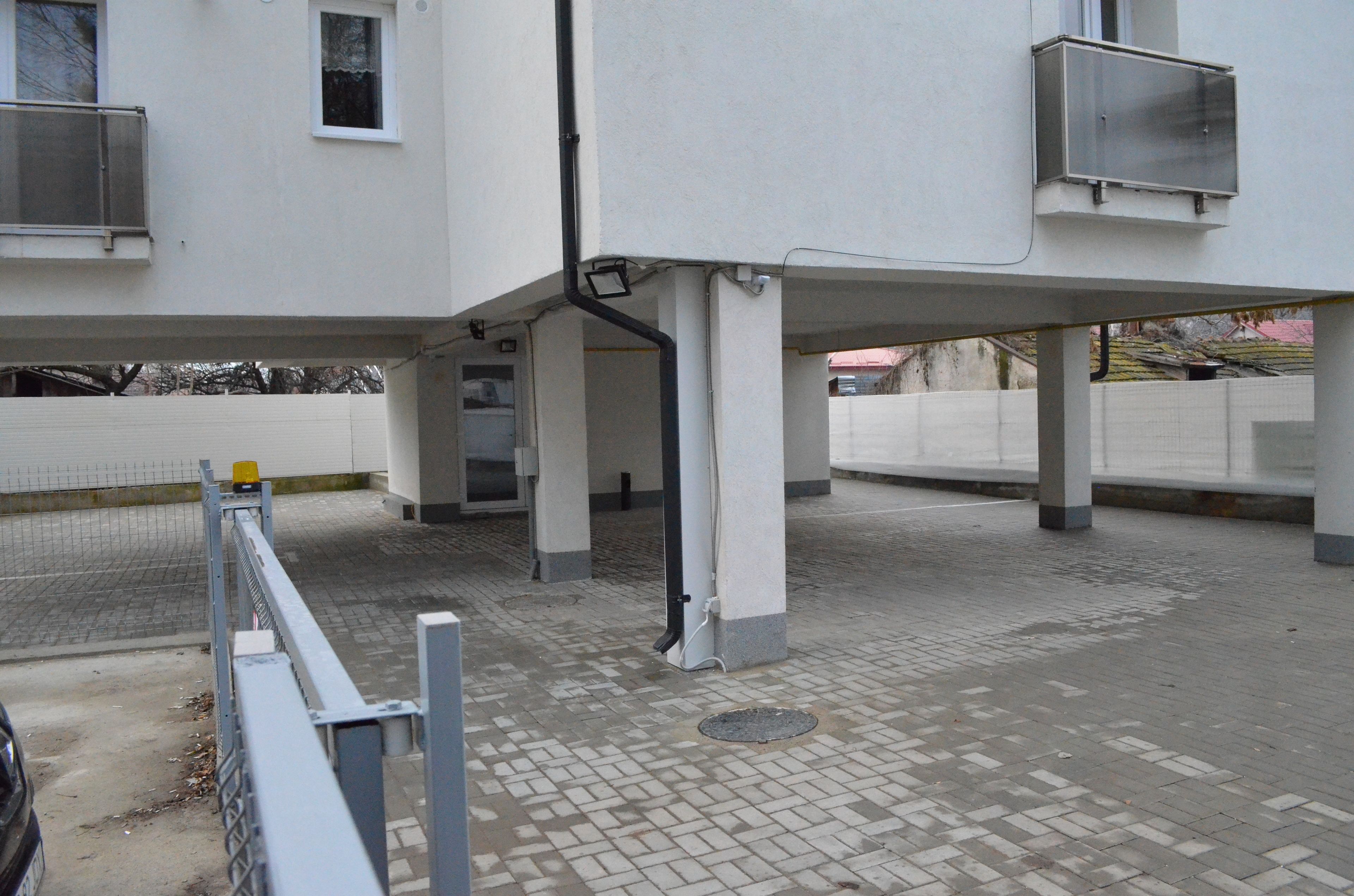 Un edificio con un piano terra piastrellato e un piano superiore bianco. Si notano elementi strutturali a vista e un tombino a livello del suolo.