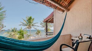 Un balcón con una hamaca, una mesa con sillas y vistas al océano y palmeras.