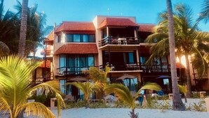 Un hotel frente a la playa con varios balcones, palmeras y una playa de arena.