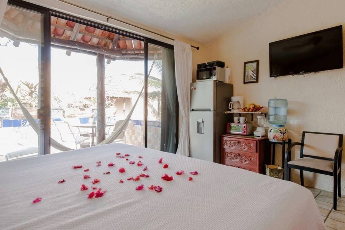 Habitación de hotel con cama, televisión, refrigerador, dispensador de agua y una pequeña mesa con cafetera.