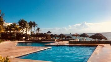 Una piscina al aire libre, sombrillas, sillones reclinables de piscina