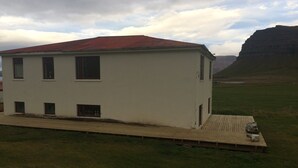 Un bâtiment blanc d’un seul étage, avec un toit rouge, un petit porche et une cour couverte d’herbe.