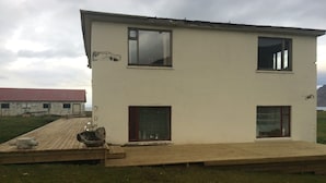 Un bâtiment à deux étages, doté d’un toit plat, d’une terrasse en bois et d’une cour gazonnée.