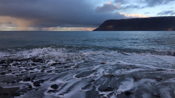 Un paysage côtier avec une rive rocheuse, des vagues et une falaise en arrière-plan.