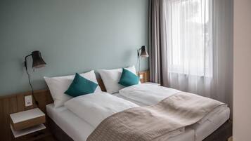 Uma cama de casal bem arrumada com almofadas brancas e azul-turquesa, um cobertor bege e duas luminárias de cabeceira.