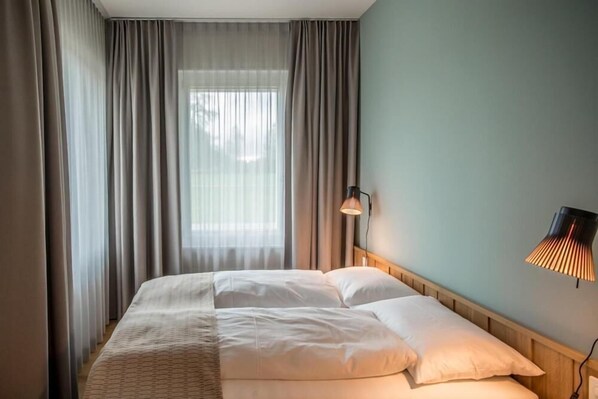 Una habitación de hotel con una cama, cortinas, una lámpara de pared y una ventana.