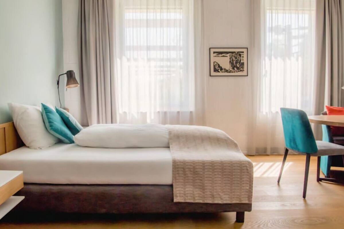 A neatly arranged hotel room with a bed, a desk, and a chair.