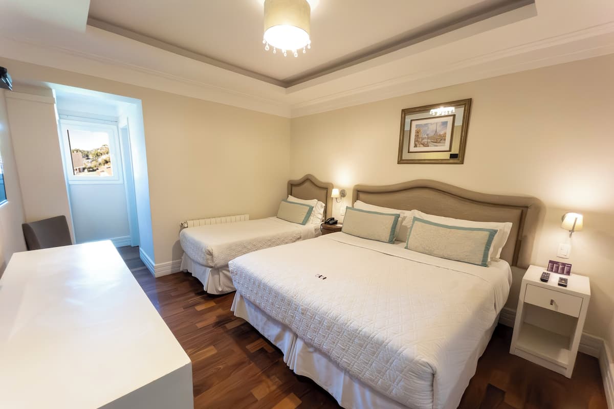 Habitación de hotel con dos camas, un escritorio, una silla, una mesita de noche con lámpara y un cuadro en la pared.