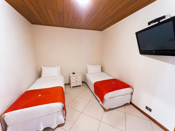 A small, clean room with two beds, a TV, and a small bedside table. - Hotel Estoril (Campos do Jordão)
