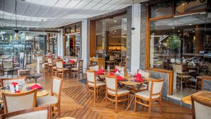 Un restaurante interior con suelo de madera, varias mesas y sillas, y amplios ventanales que dan a la calle.