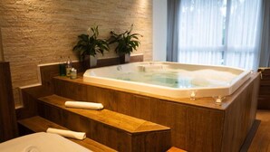 Un baño moderno con pared de piedra, una bañera grande, bancos de madera y plantas en macetas.