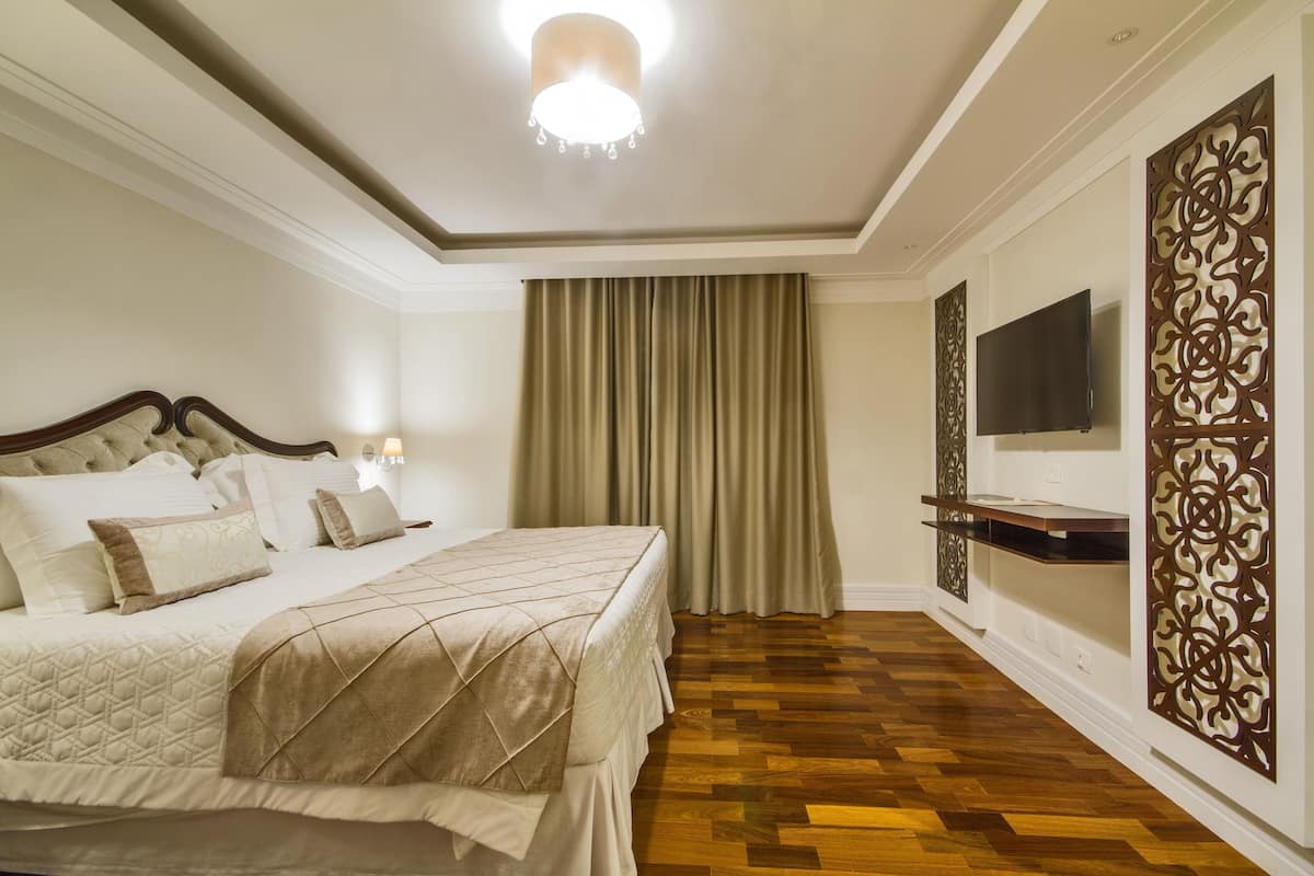 Un dormitorio con cama, cortinas, televisor y un separador decorativo.