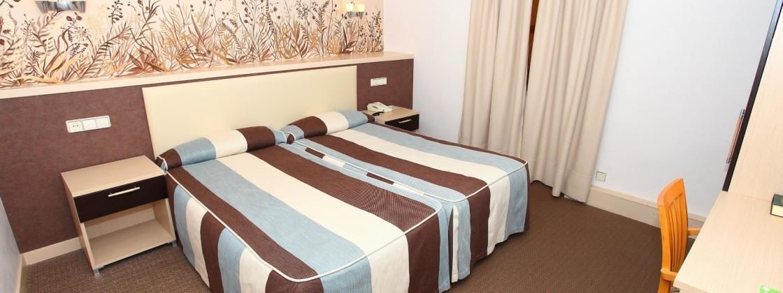 A hotel room with two beds, a nightstand, a desk, and a wall-mounted telephone.