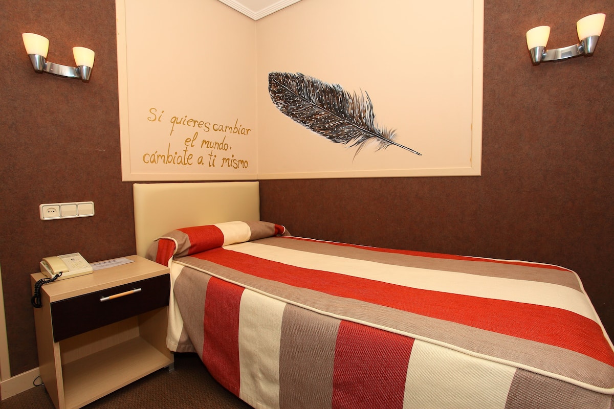 A hotel room with a bed, bedside table, and a wall with a feather artwork and a motivational quote.