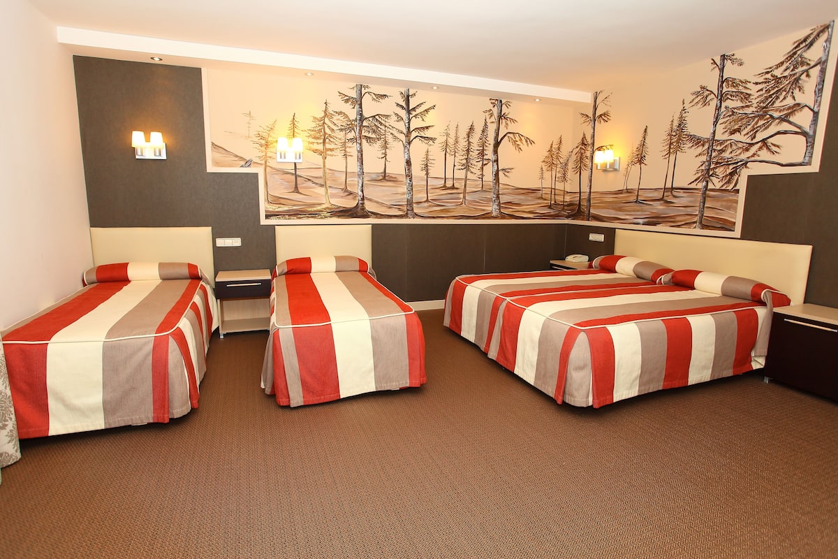 A hotel room with two single beds, a large painting of trees on the wall, and a carpeted floor.