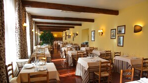 A restaurant with wooden beams, striped tablecloths, and framed pictures on the walls. - Hotel Monasterio de Leyre (Yesa)