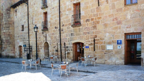 A stone building with outdoor seating, a wooden door, and a sign indicating a hotel. - Hotel Monasterio de Leyre (Yesa)