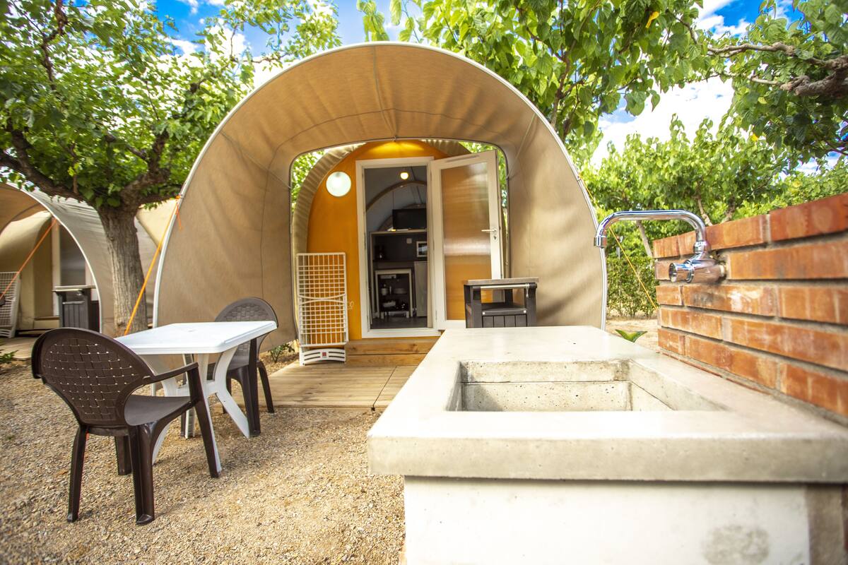Un espacio al aire libre cubierto con una mesa, sillas, una jardinera de concreto y un muro de ladrillo.