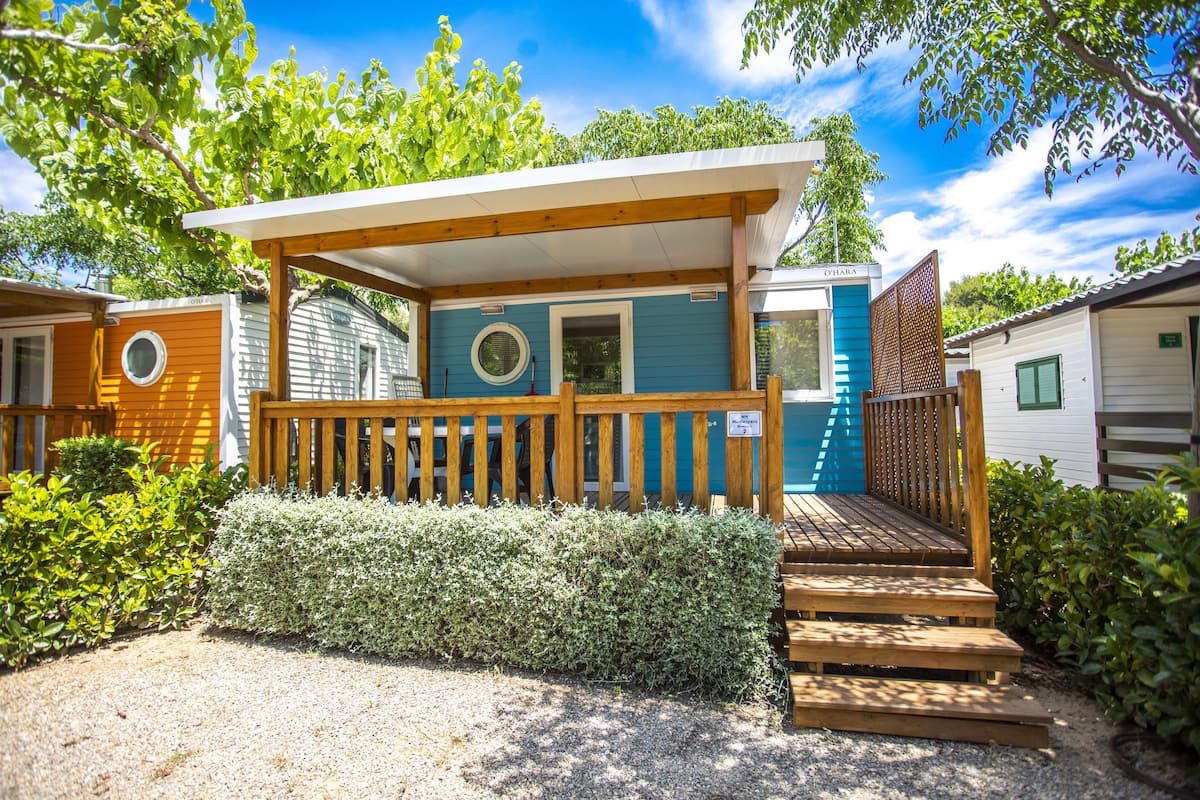 Una casa móvil pequeña de un piso, con un porche y una pequeña terraza.