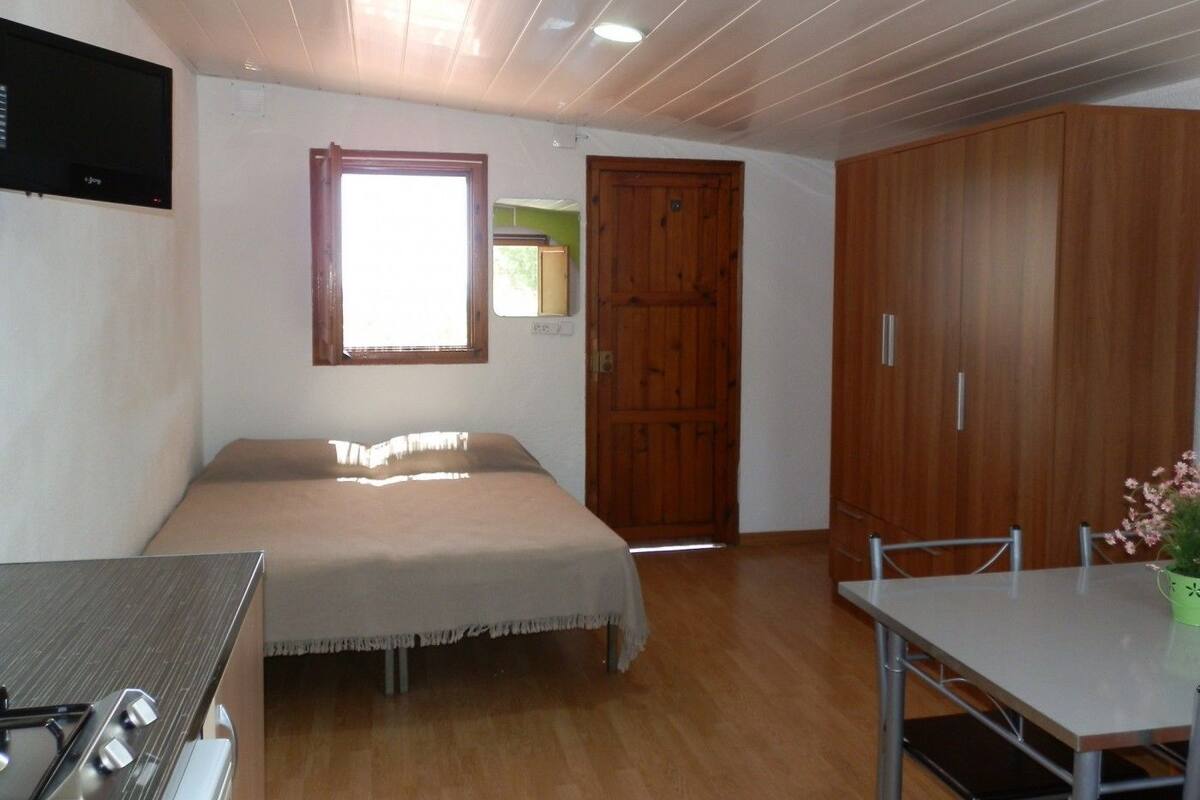 Un dormitorio con una cama, un armario de madera, una mesita y un televisor montado en la pared.
