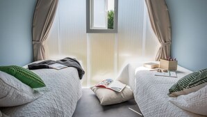 Une chambre confortable avec deux lits, une fenêtre et une petite table sur laquelle se trouvent des livres et une tasse.