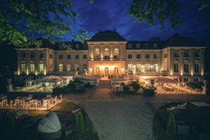 Ein großes, gut beleuchtetes Gebäude mit einer symmetrischen Fassade, zahlreichen Fenstern und einem zentralen Eingang mit Stufen.