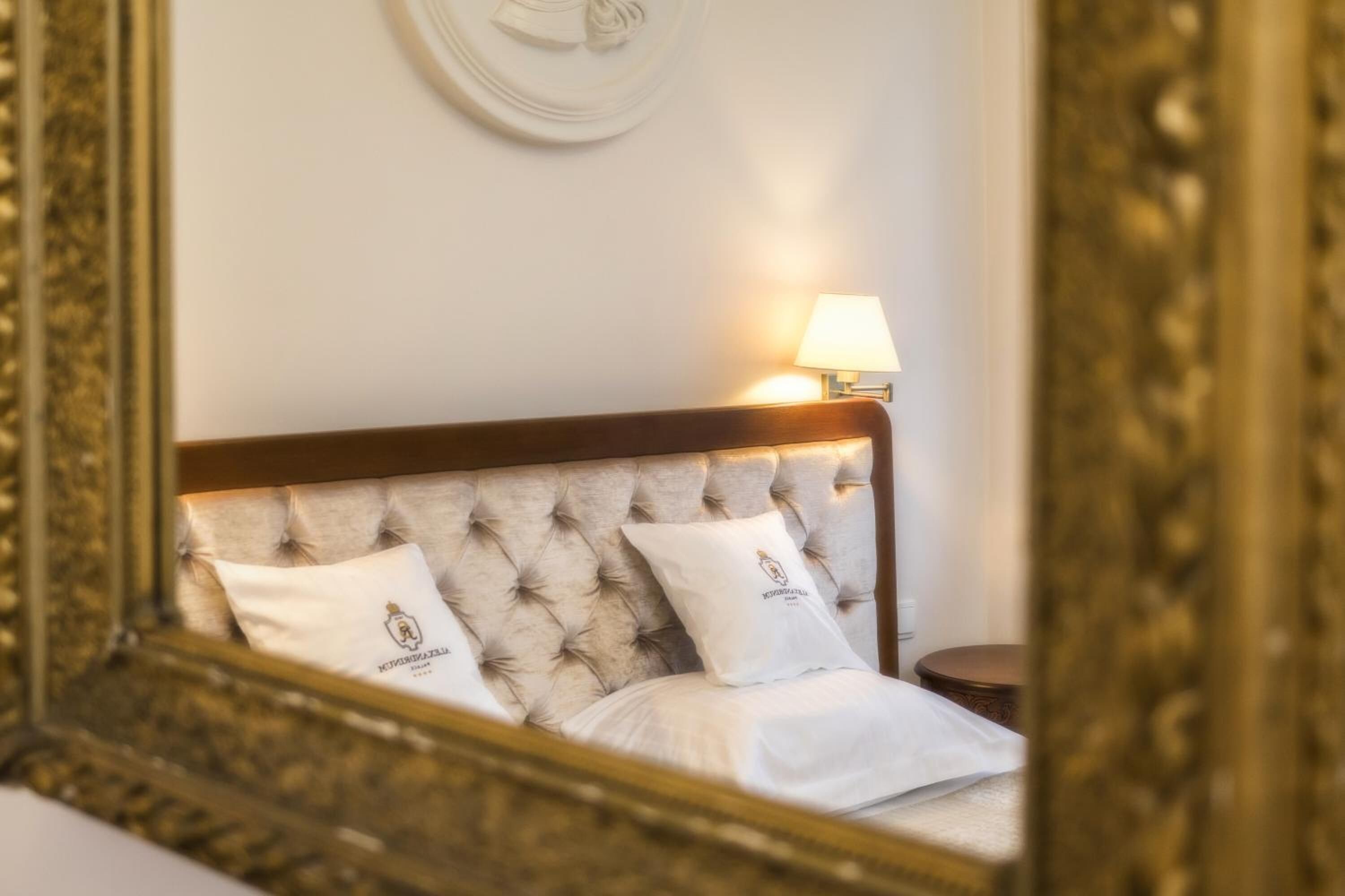 A neatly made bed with a tufted headboard and two pillows, a bedside lamp, and a round wooden nightstand.