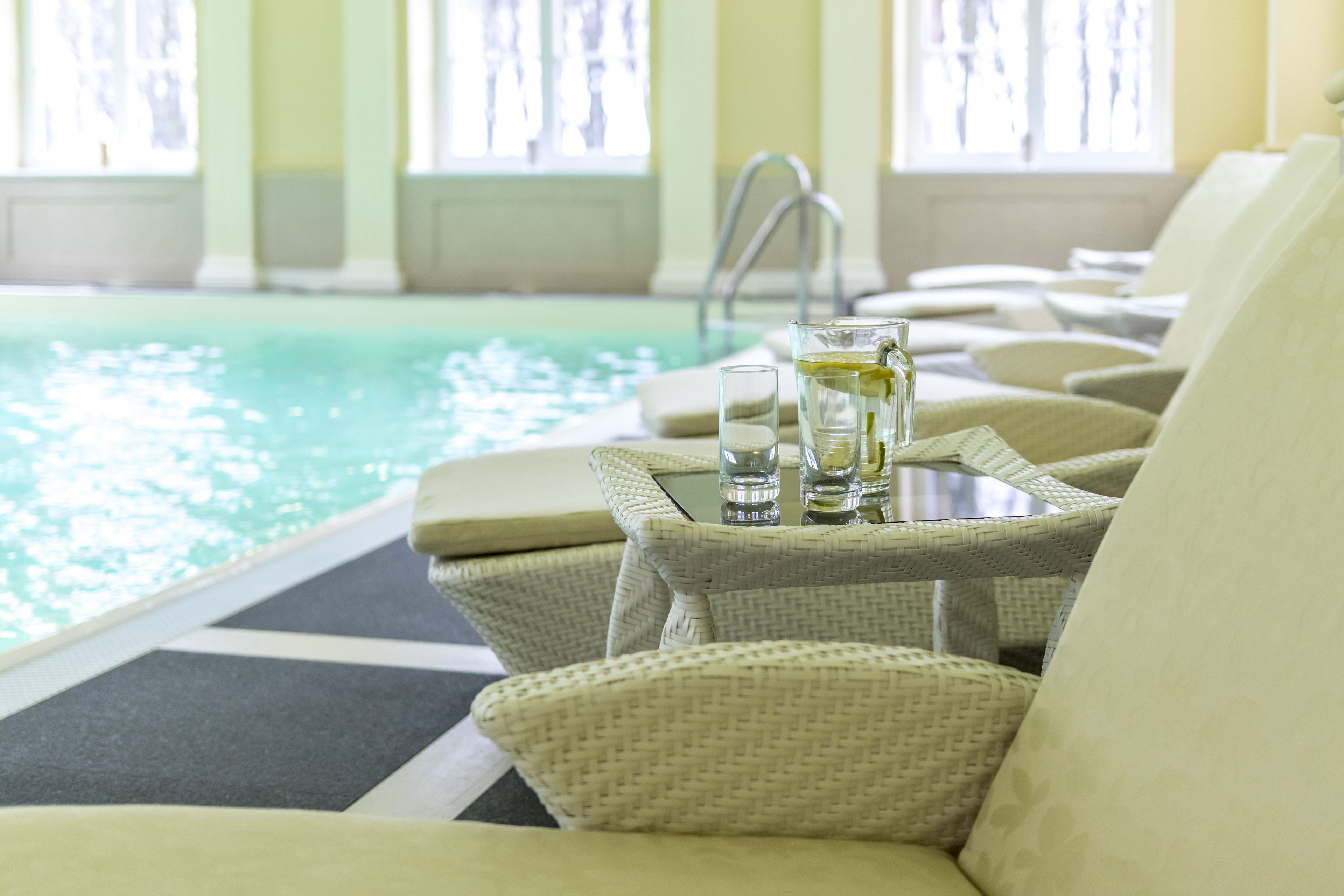 A poolside lounge area with wicker chairs and a glass table with drinks.