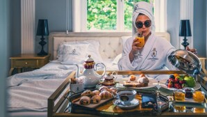 Een hotelkamer met een bed, een ontbijttafel met gebak, een theepot en een schaal fruit.