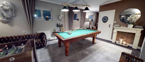 Una sala de billar con mesa de billar, mesa de fútbol de mesa y chimenea.