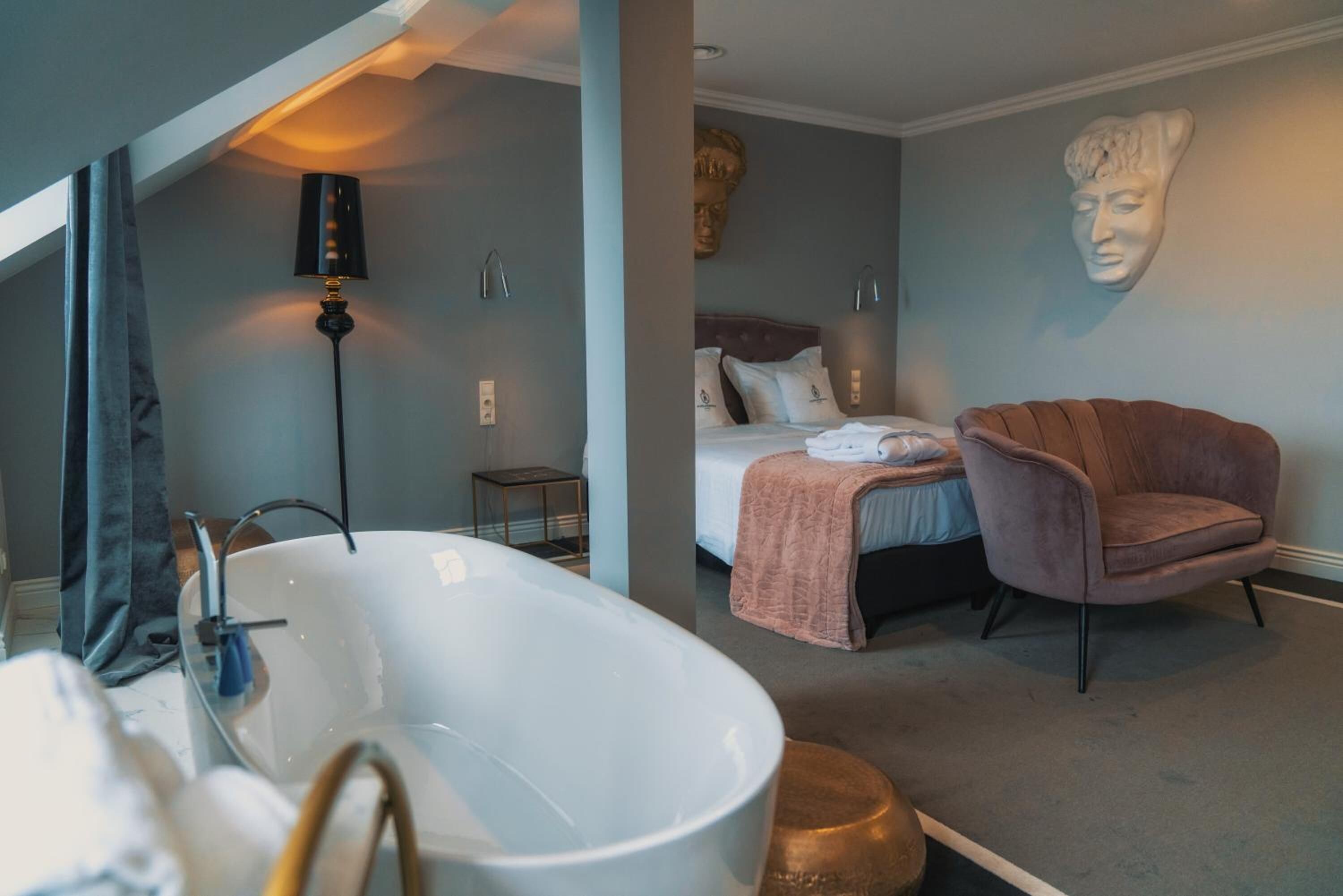 A modern bathroom with a freestanding bathtub, a small bedside table, and a wall-mounted sculpture.