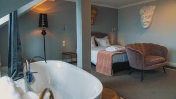 A modern bathroom with a freestanding bathtub, a small bedside table, and a wall-mounted sculpture.