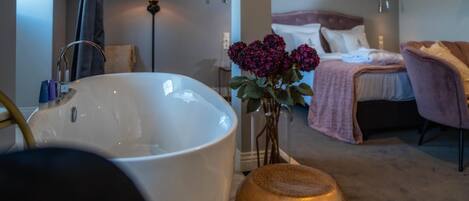 A bathroom with a large white bathtub, a golden decorative bowl, and a vase with purple flowers.