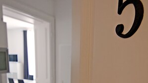 Une pièce dont le mur porte le numéro « 5 », un coin cuisine avec un plan de travail foncé, et un coin repas avec des chaises et une table à l’arrière-plan.