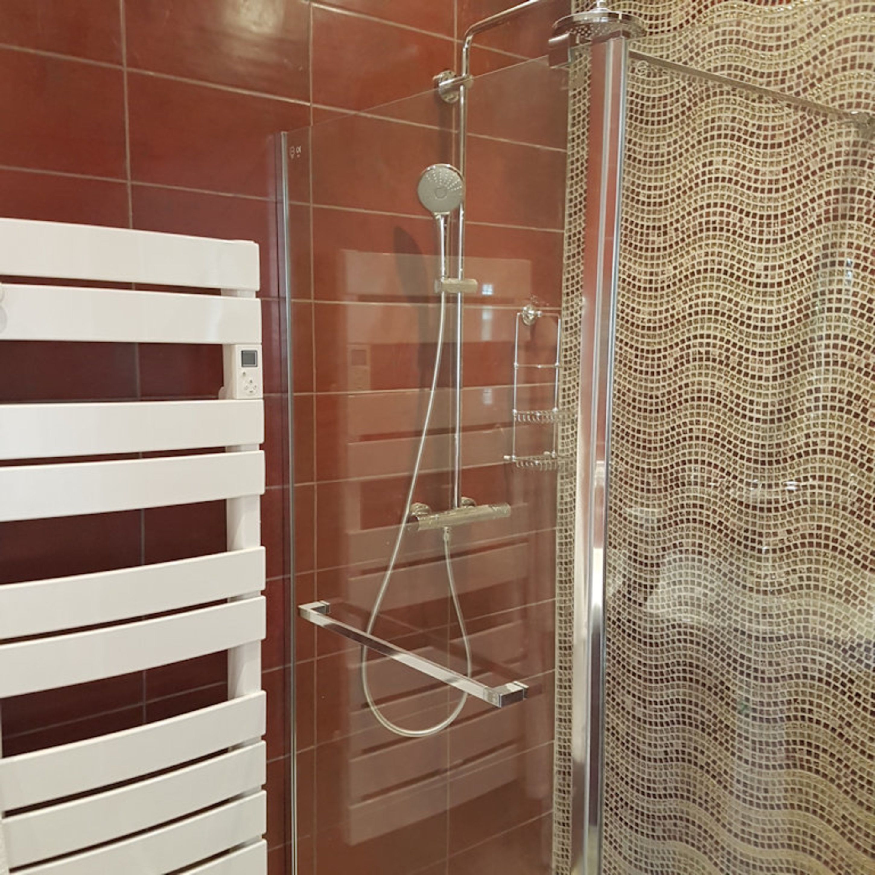 Une douche fermée par des parois de verre, dotée d’un robinet et d’un panneau de commande en chrome, d’un porte-serviettes blanc et d’un rideau de douche texturé.