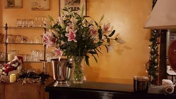 A bar area with a metal bar counter, a vase with flowers, and shelves with glasses and bottles.