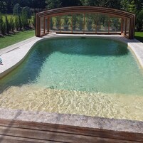 Una piscina cristalina con muelle de madera y cerramiento de vidrio.