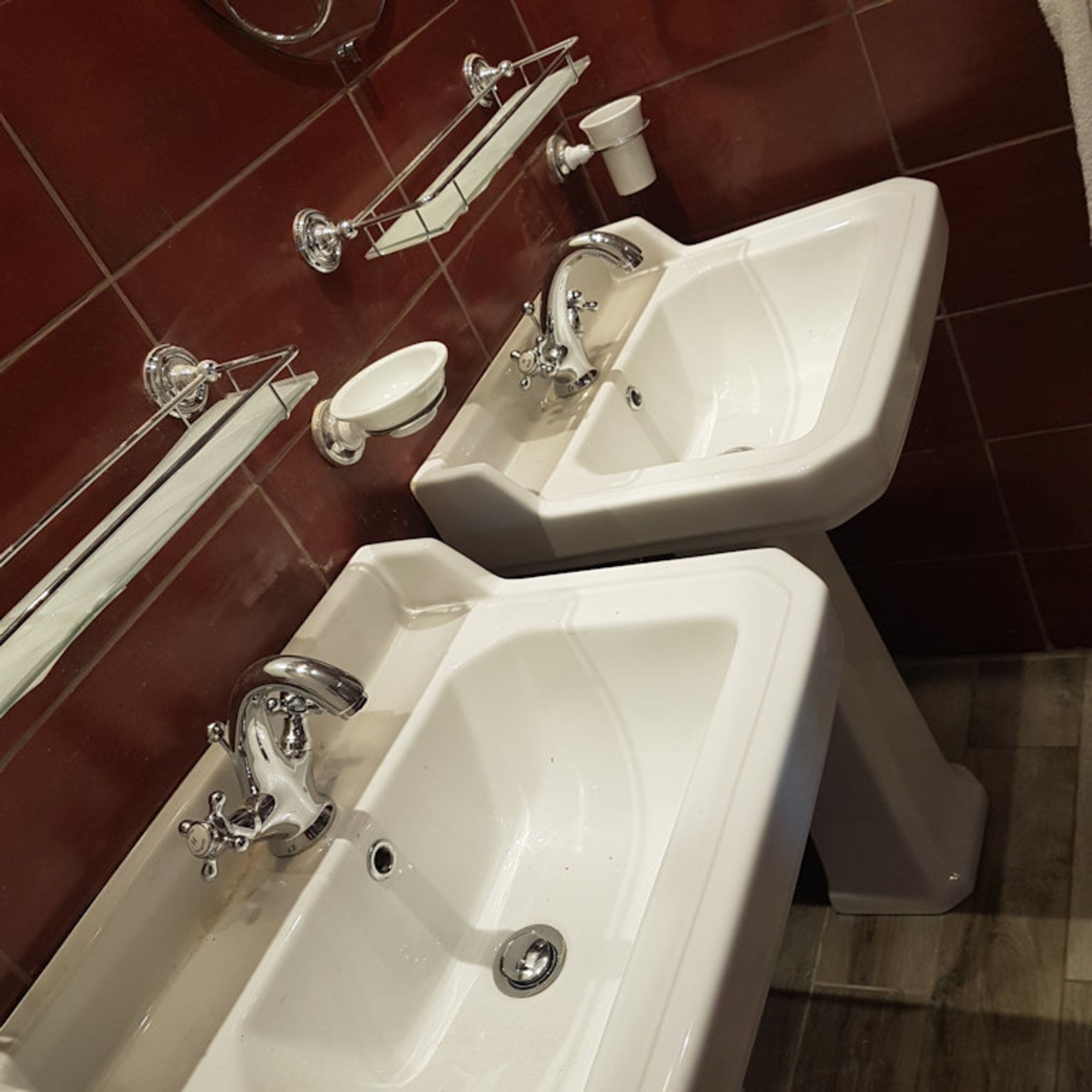 Due lavandini bianchi con accessori cromati in un bagno dalle pareti piastrellate di rosso.