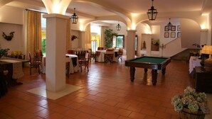 Un vaste espace intérieur comprenant une table de billard, des tables et des chaises, avec des plafonds en arc de cercle et un éclairage chaleureux.