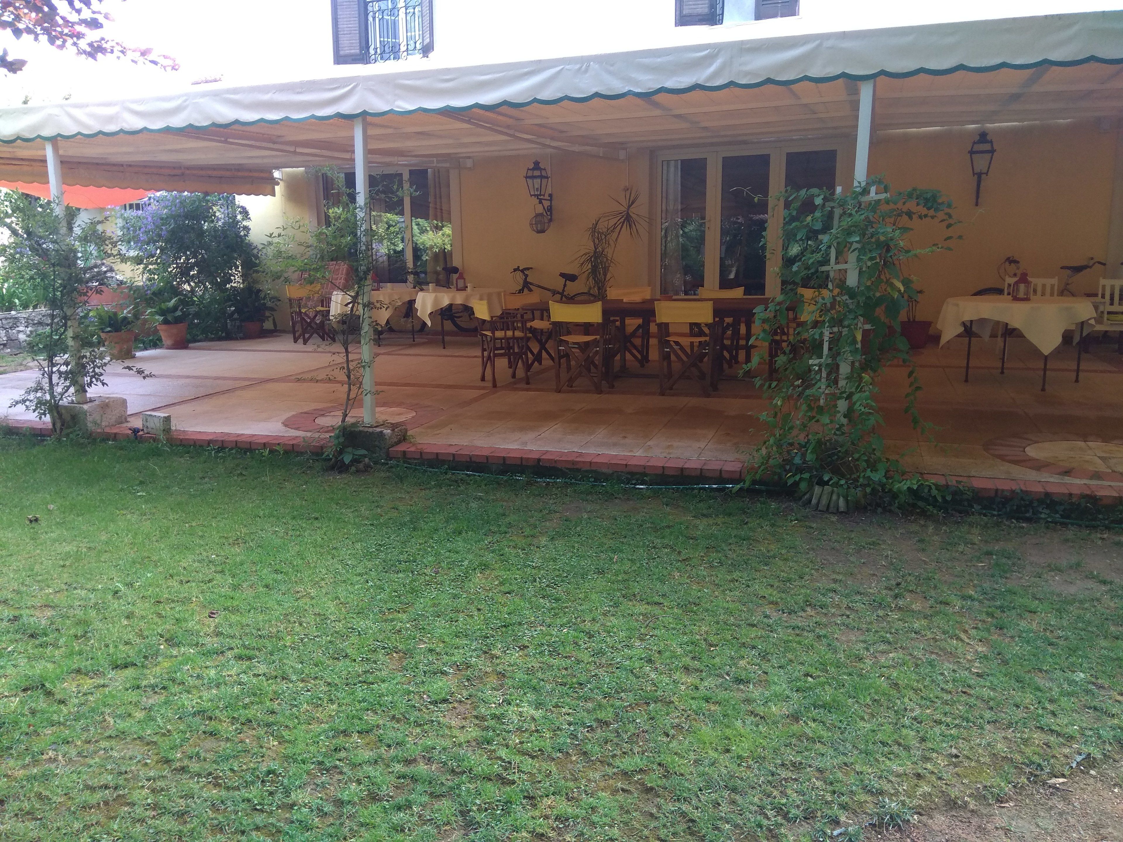 An outdoor dining area with tables and chairs, surrounded by potted plants and a covered walkway.