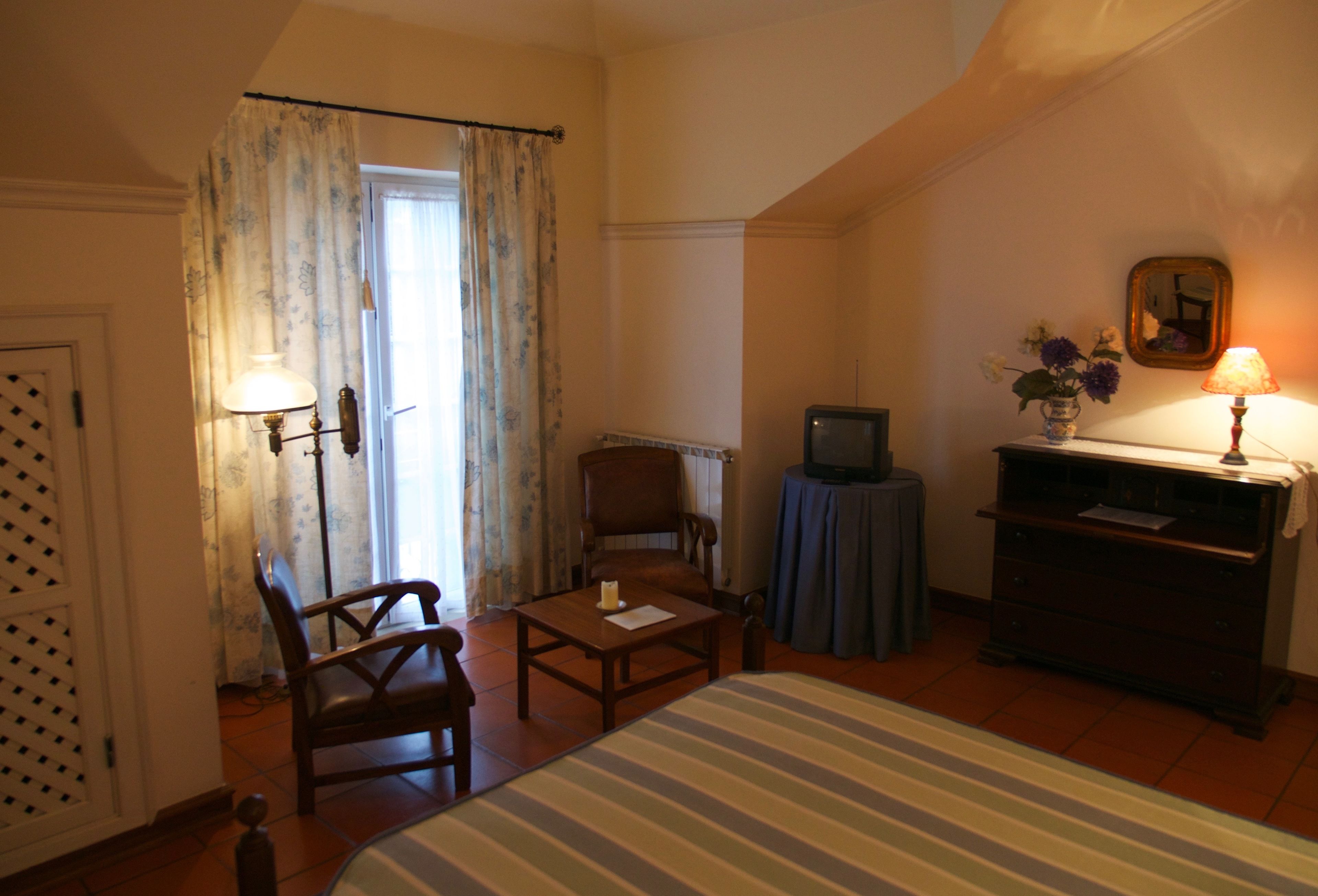 Une chambre d’hôtel avec un lit, une chaise, une petite table, un téléviseur et une commode.