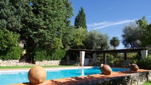 Une piscine aux murs en pierre et aux grands pots décoratifs, entourée d’une végétation luxuriante et d’un bâtiment en pierre.