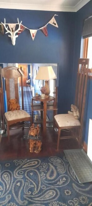 Una habitación con pared azul, una silla de madera, un tapete pequeño y una lámpara.