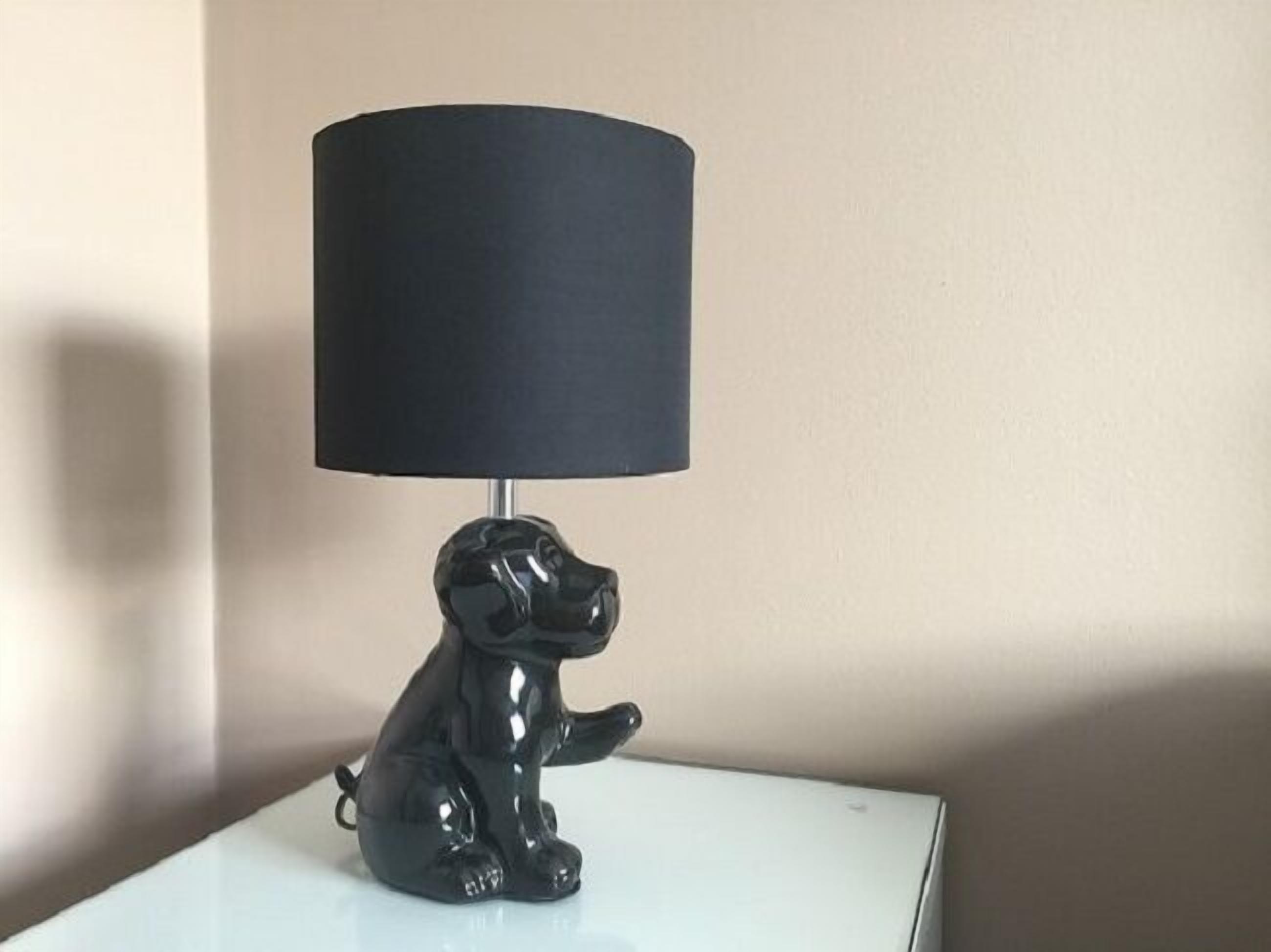 A black dog-shaped lamp with a cylindrical shade on a white surface.