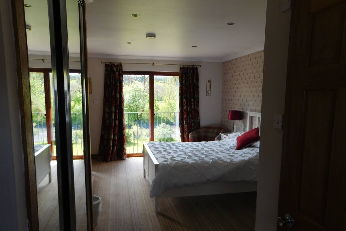 A bedroom with a large bed, a chair, a nightstand, and a view of a balcony.