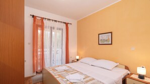 Una habitación de hotel con cama, una mesita de noche con lámpara, un cuadro en la pared y una ventana con cortinas.