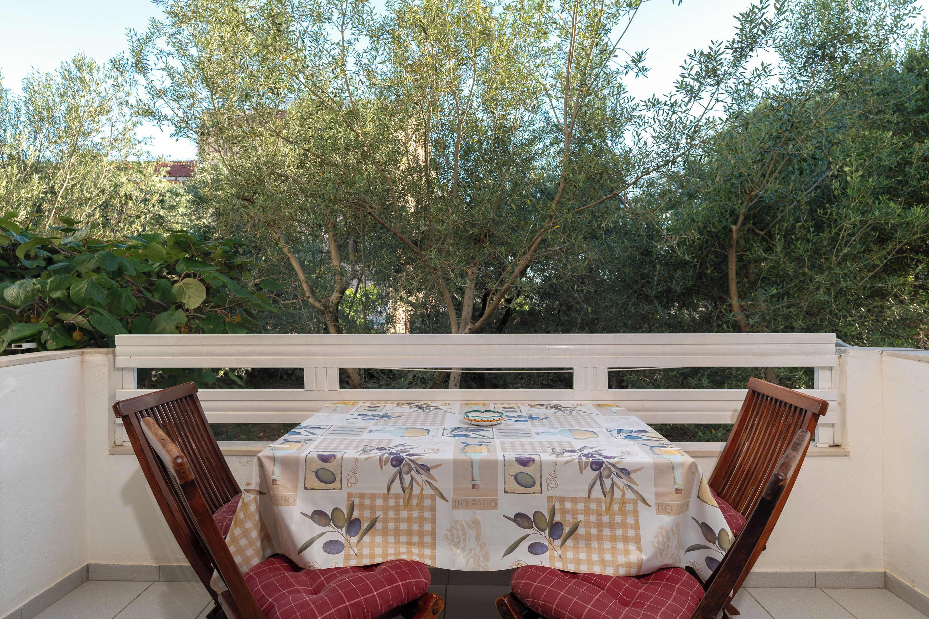 Ein Balkon mit Tisch und Stühlen, umgeben von Bäumen.