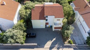 An aerial view of a residential building with a tiled roof, a paved driveway, and surrounding greenery.