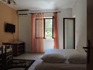 Un dormitorio con cama, televisor, ventana con cortinas y una puerta.
