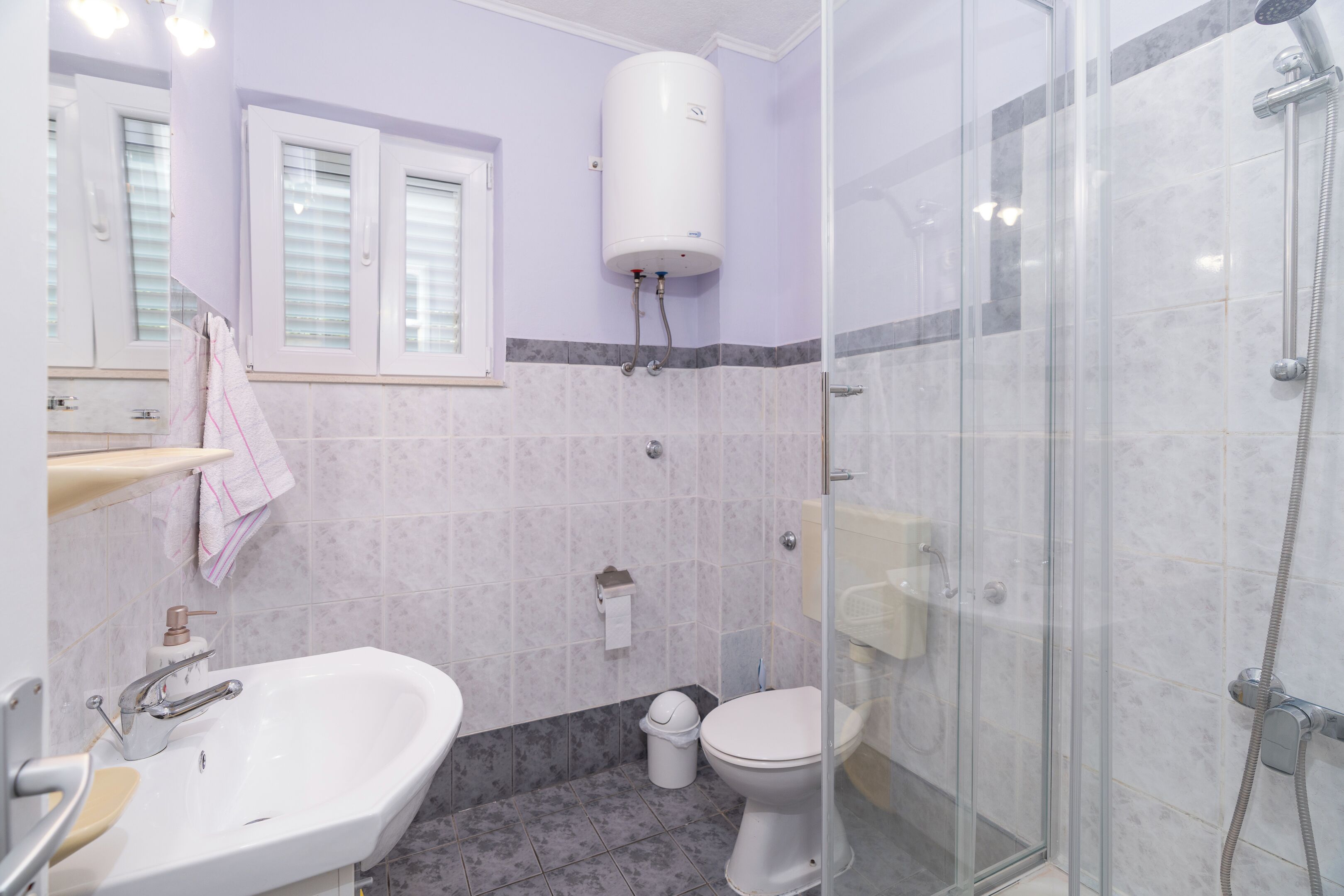 Une salle de bain équipée d’un lavabo, de toilettes, d’une douche et d’un chauffe-eau blanc fixé au mur.